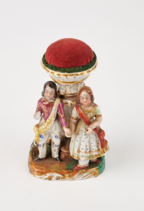 Nadelkissen mit Figurengruppe: Kissenkuppel auf Säule, davor ein mit Schärpen bekleidetes Paar auf Sockel